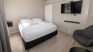 A bedroom with a bed, a TV mounted on the wall, a chair, and a wardrobe. - Steinaskjól Apartments - Strandgata (Akureyri)