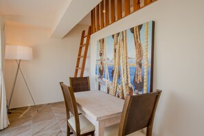 Un coin repas avec une table et des chaises en bois, un tableau représentant des cordes accroché au mur et un lampadaire.