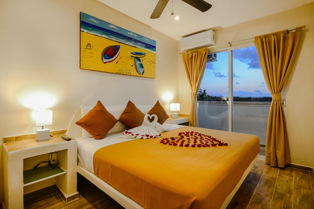 Habitación de hotel con cama, mesita de noche, lámpara, un cuadro en la pared y vistas a través de la ventana.