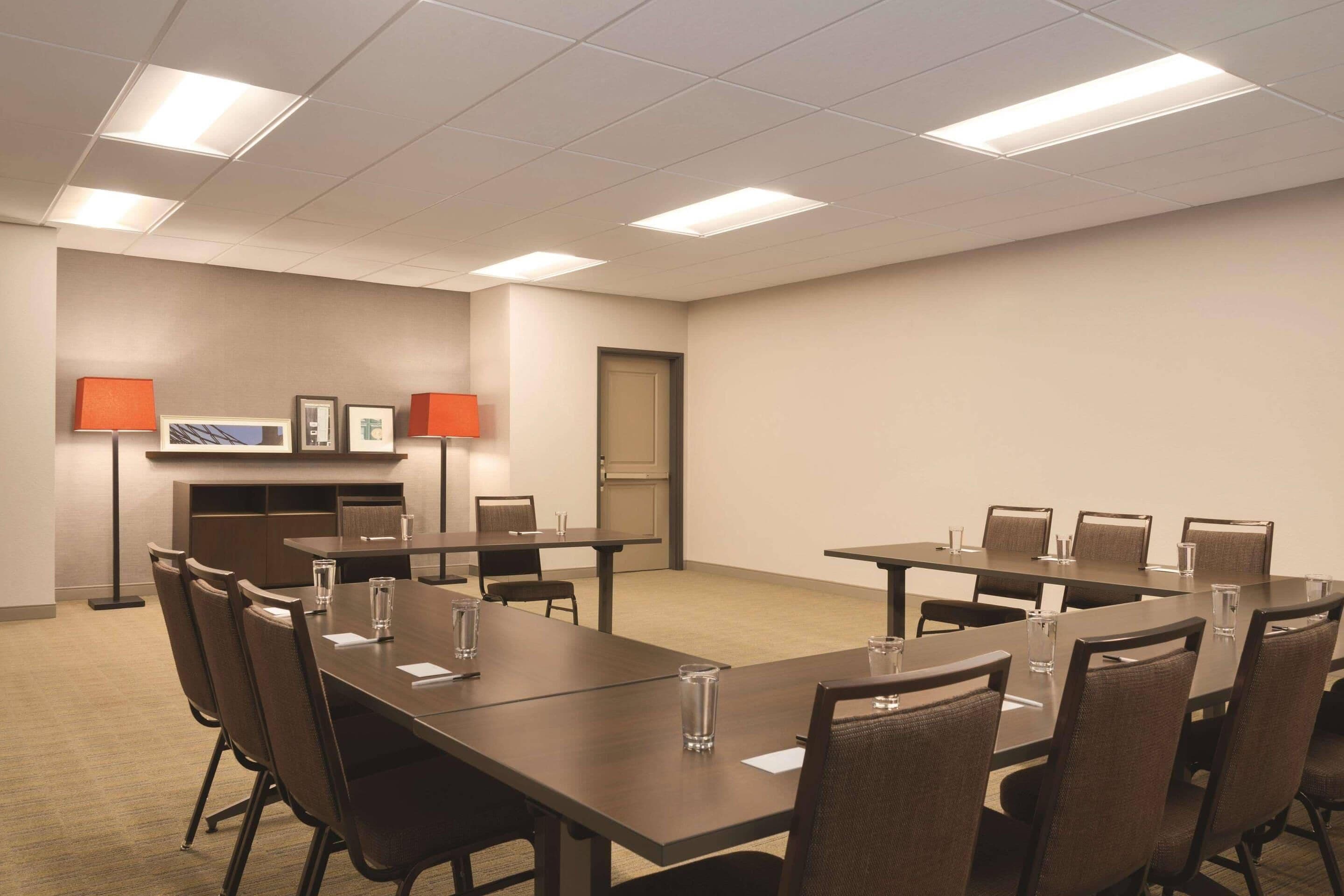 A conference room with multiple tables and chairs, equipped with lamps and a flat-screen TV.