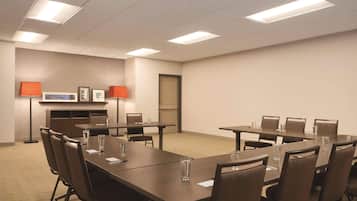 Una sala conferenze con diversi tavoli e sedie, dotata di lampade e un televisore a schermo piatto.