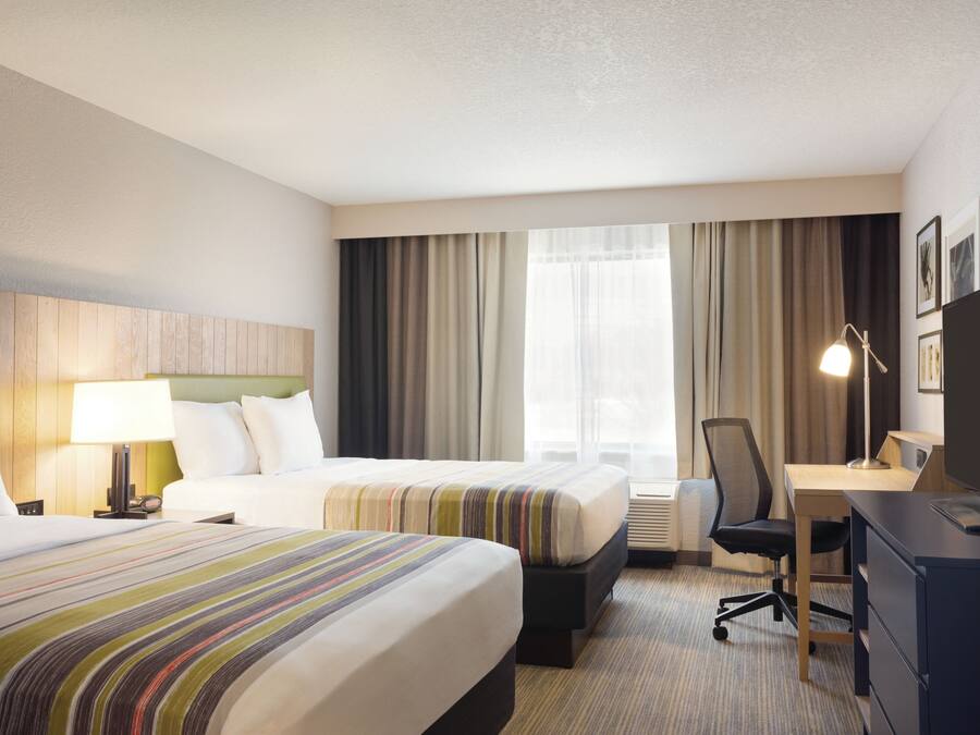 Habitación de hotel con dos camas, un escritorio, una silla, un televisor y una lámpara.