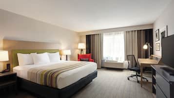 A hotel room with a large bed, a desk, a chair, a TV, and a window with curtains.