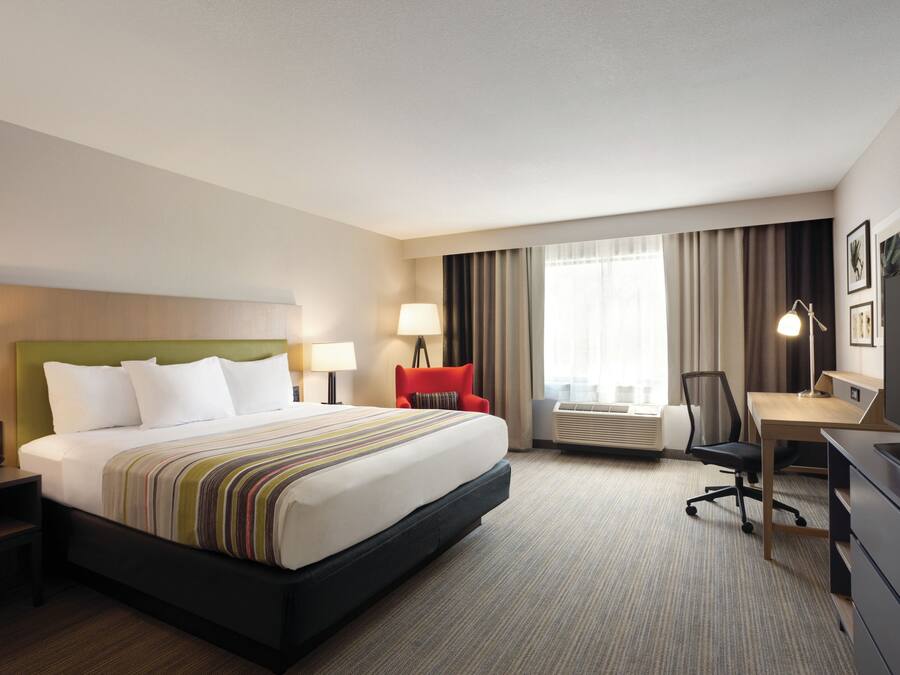 A hotel room with a large bed, a desk, a chair, a TV, and a window with curtains.