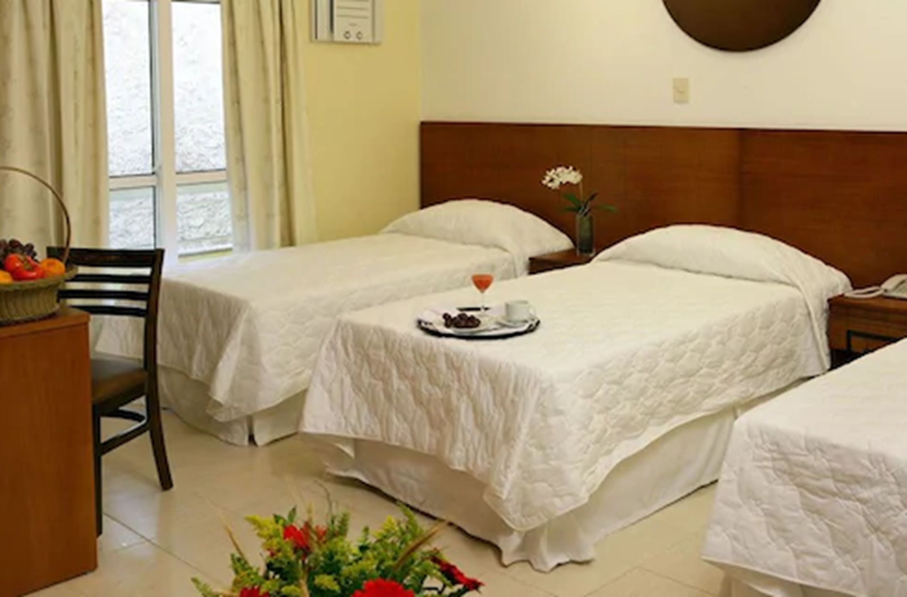 A hotel room with two single beds, a small table with a tray of food, a chair, and a vase with flowers.