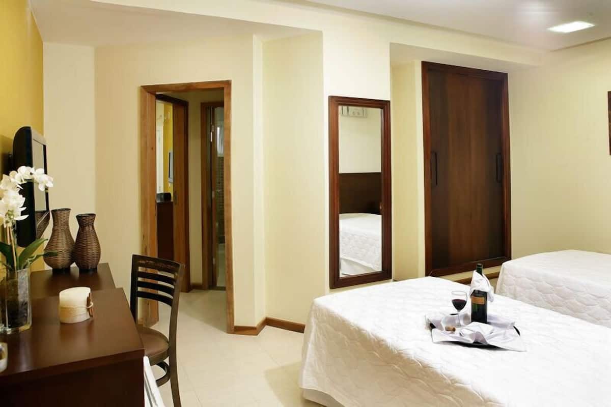 Ein Hotelzimmer mit zwei Betten, einem Esstisch mit Stühlen, einer Vase mit Blumen und einem Tablett mit Flasche und Gläsern.