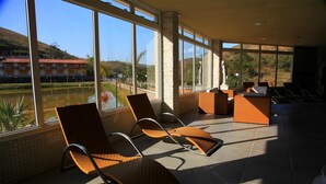 A sunlit indoor seating area with large windows overlooking a body of water and a distant building. - Vassouras Eco Resort (Vassouras)