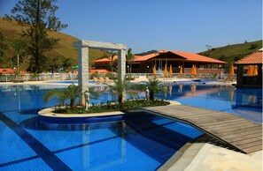 Una piscina con muelle de madera, palmeras y un edificio con tejado rojo al fondo.