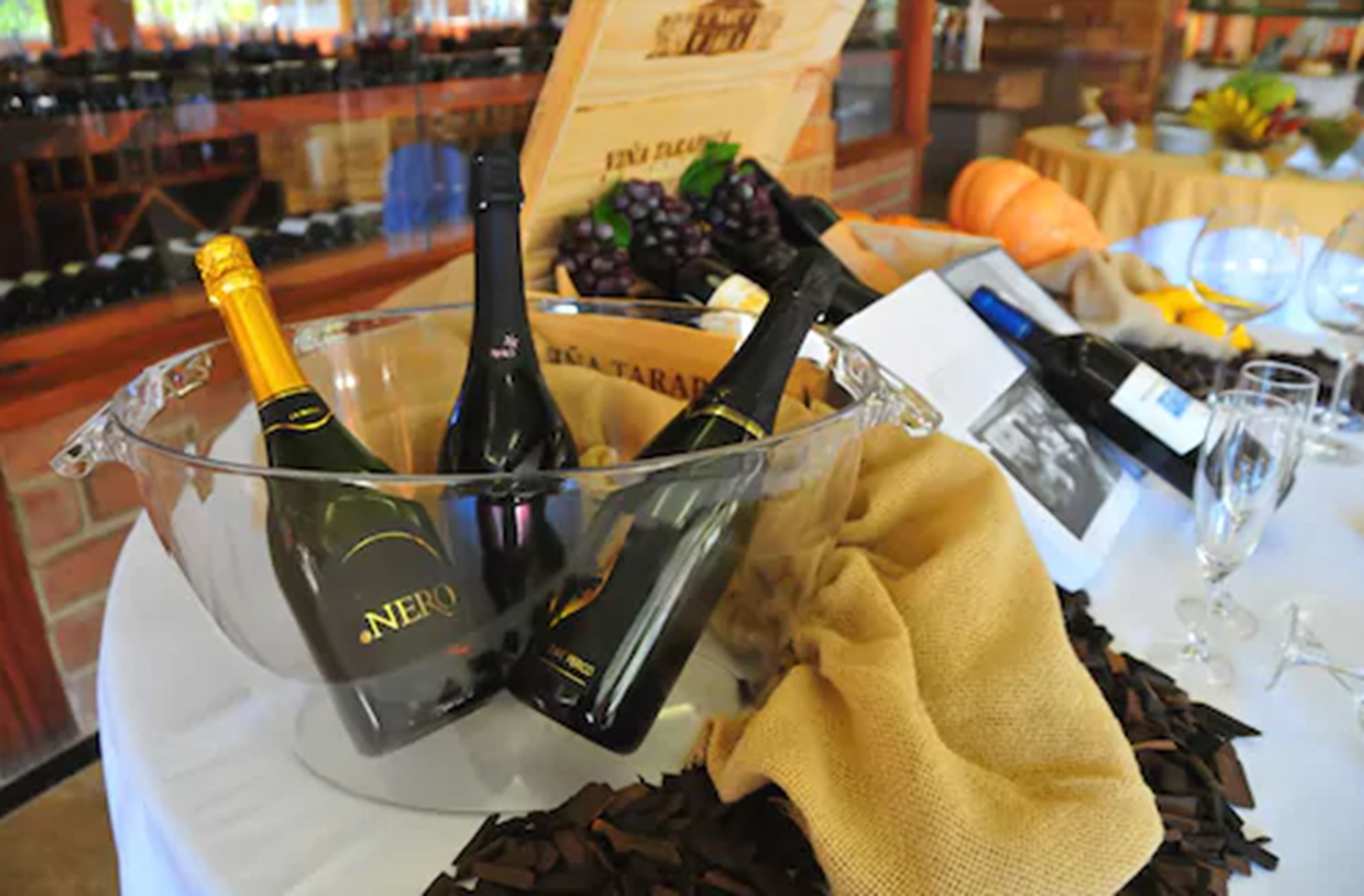 A bar area with a large glass bowl containing bottles of wine, a bottle of champagne, and a wine bottle on a table.