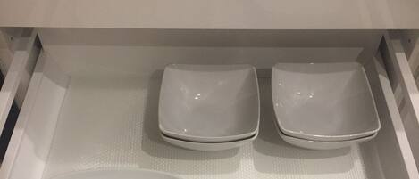 A drawer with three white plates and a larger white bowl.