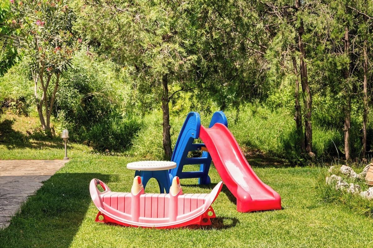 Ein Spielplatz mit einer Rutsche, einem kleinen Tisch und einer sitzförmigen Schaukel in Bootsform.