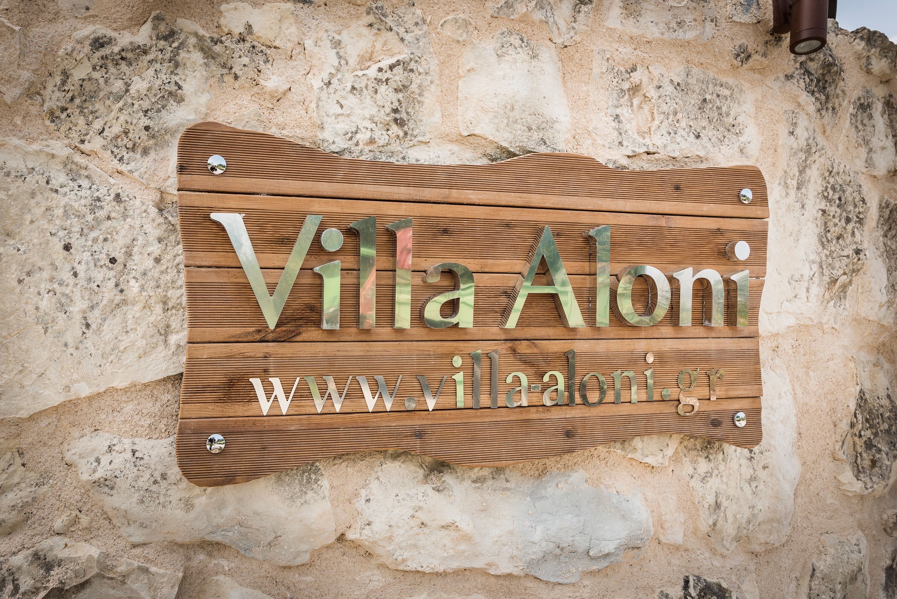 A wooden sign with the text "Villa Aloni" and a website address.