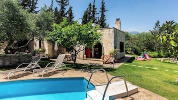 Relax by the serene pool surrounded by lush greenery and a rustic stone structure.