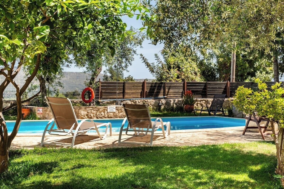 En trädgård med en pool, två solstolar, ett litet träd och en stenmur.