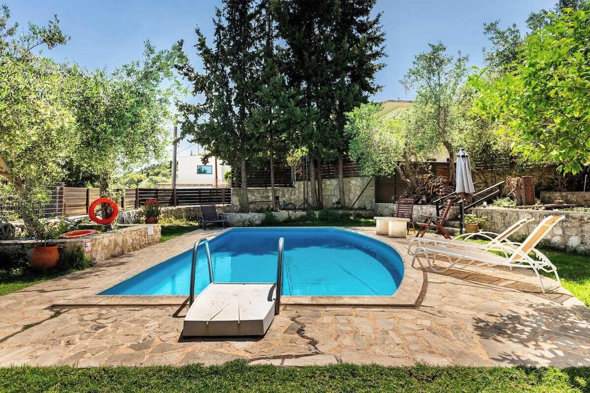 Une piscine rectangulaire dotée d’un plongeoir, entourée de carreaux de pierre, de plantes en pot et de mobilier d’extérieur.