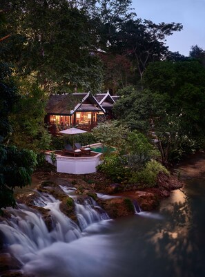 Un chalet isolé, avec une cascade, entouré d’une forêt dense.