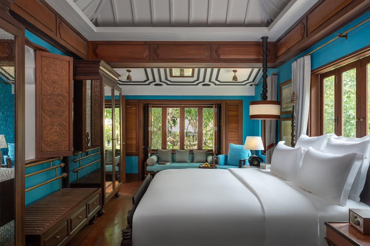 Une chambre spacieuse avec un grand lit, un coin salon offrant une vue sur la verdure et une armoire en bois.