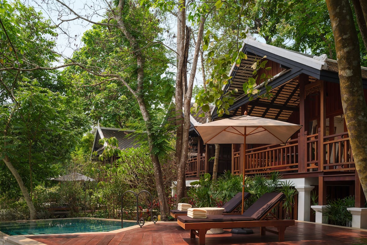 Une terrasse en bois avec une piscine, des chaises longues et un espace abrité avec un parasol.