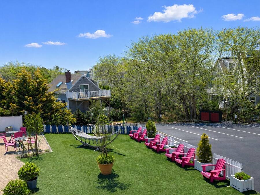 A residential property with a backyard featuring a hammock, pink Adirondack chairs, a white picket fence, and a small garden.