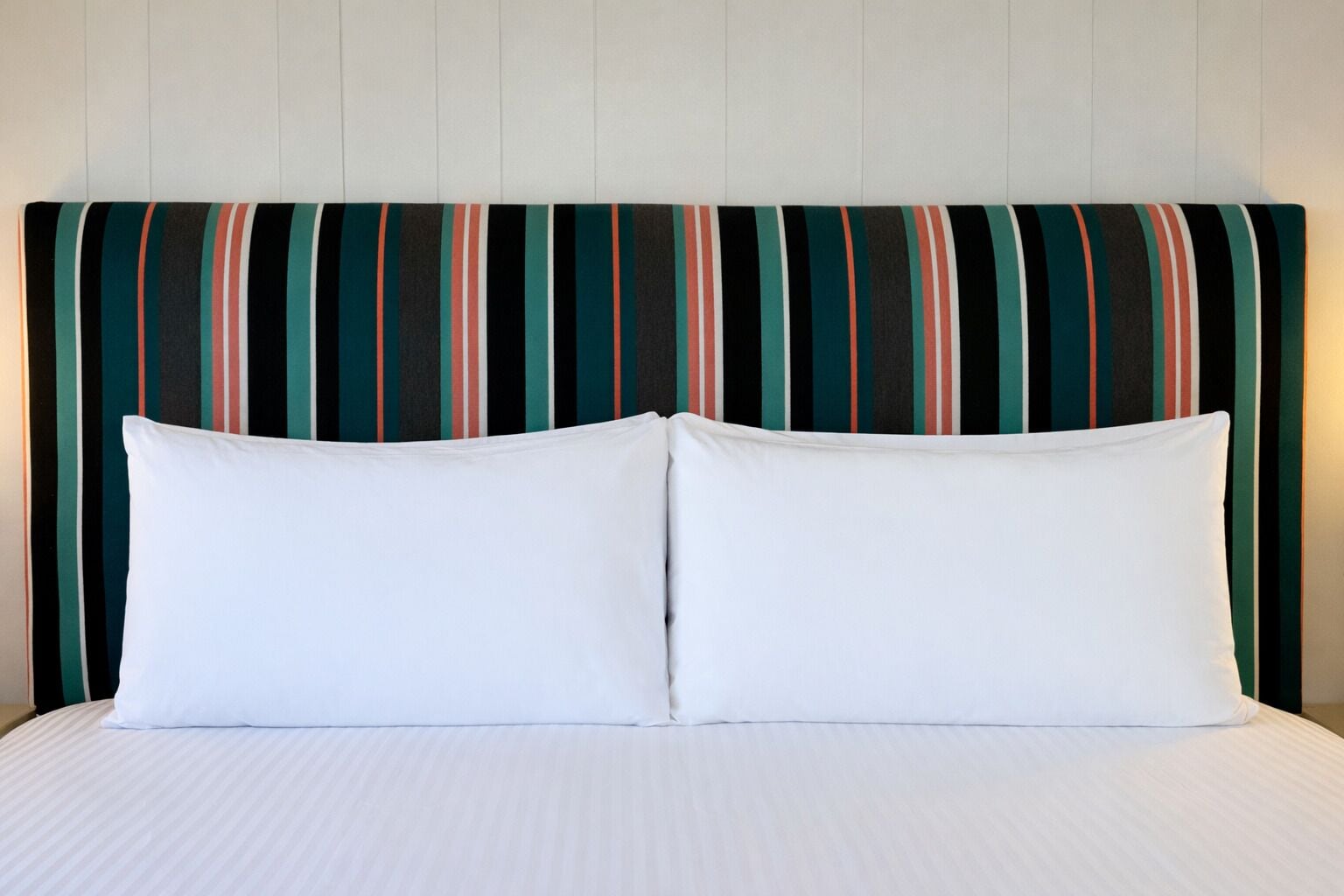 A bed with white bedding and two pillows, a striped headboard, and a plain wall.