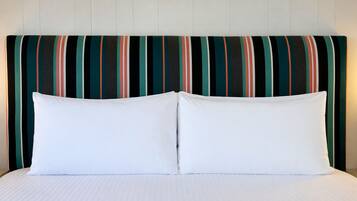 A bed with white bedding and two pillows, a striped headboard, and a plain wall.