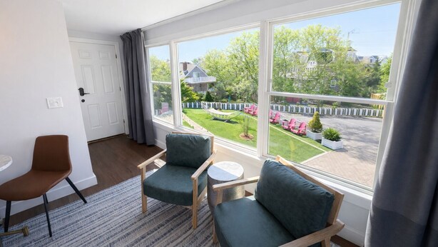 A room with a large window, two green upholstered chairs, a small round table, a brown chair, and a patterned rug. - The Foxberry - A Digital Concierge Guesthouse (Provincetown)