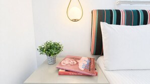 A neatly made bed with a striped pillow and a white pillow, a bedside table with a small potted plant and two books, and a wall-mounted light fixture. - The Foxberry - A Digital Concierge Guesthouse (Provincetown)