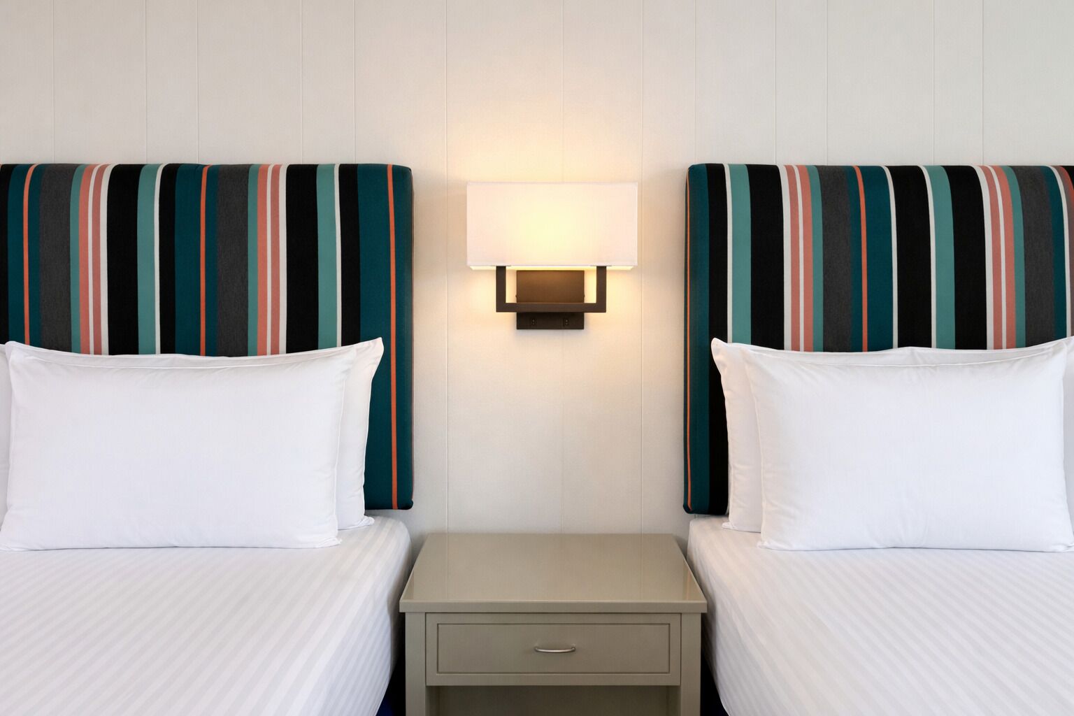 Een hotelkamer met twee bedden, een nachtkastje en een wandlamp.
