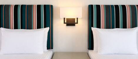 A hotel room with two beds, a nightstand, and a wall-mounted lamp.