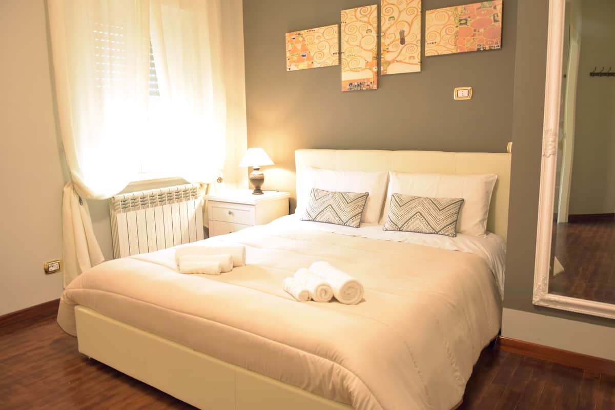 A neatly made bed with pillows, a bedside lamp, and a radiator.