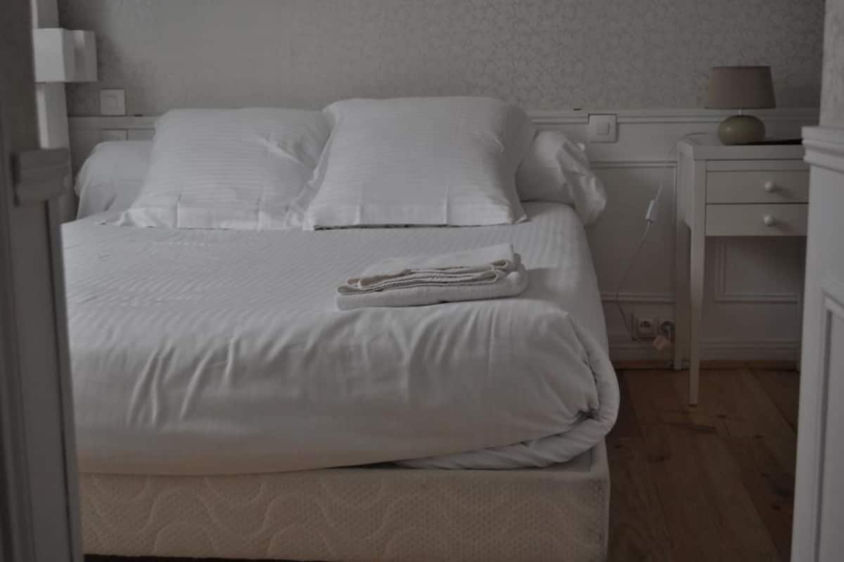 A neatly made bed with white linens and a folded towel on the side.