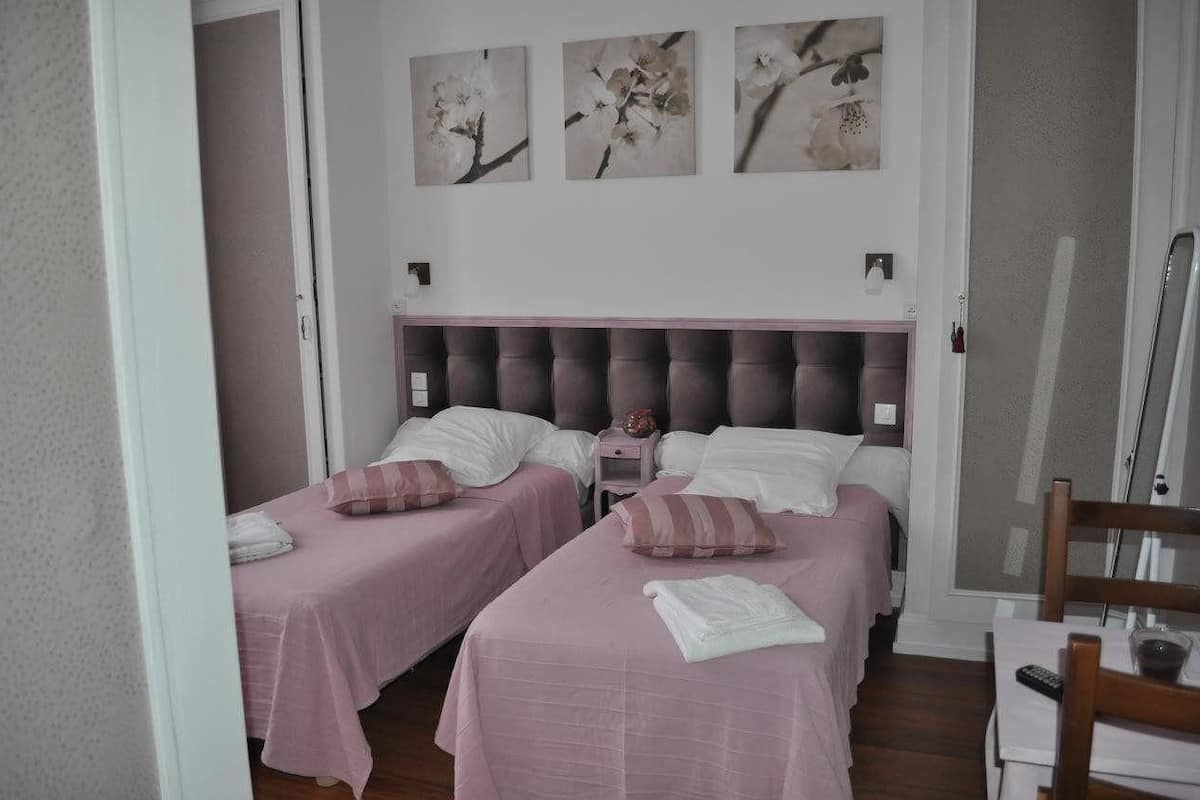 A bedroom with two beds, each with pink bedding and a tufted headboard. There are three wall-mounted paintings above the beds.