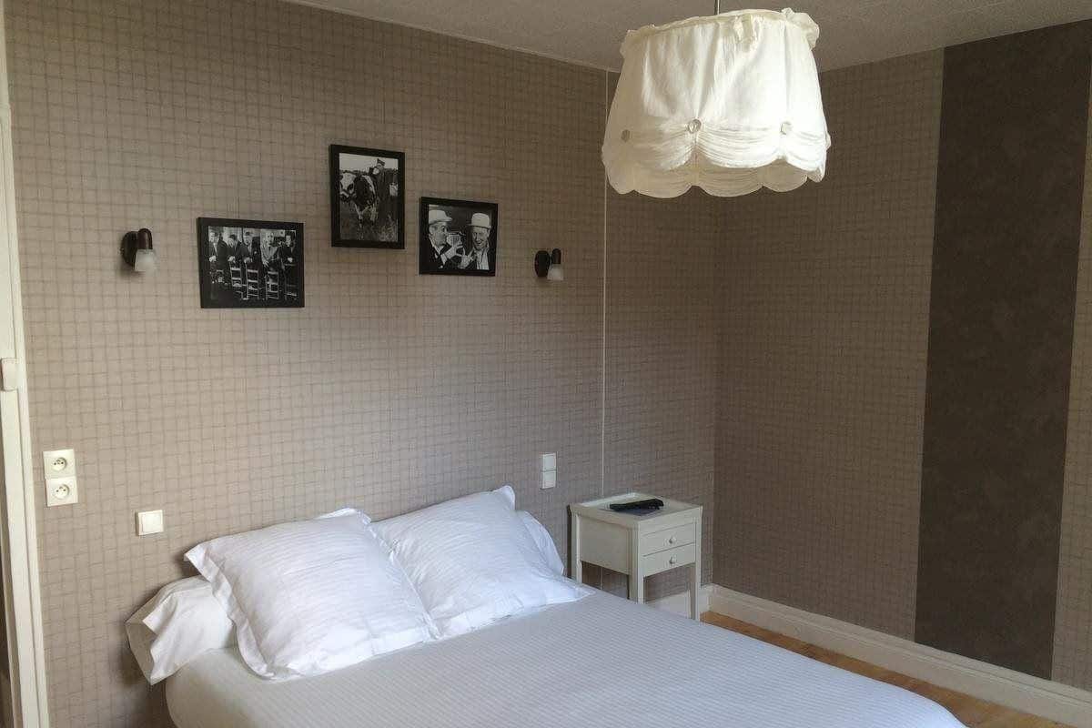 A neatly made bed with white linens in a room with a grid-patterned wall and a hanging light fixture.