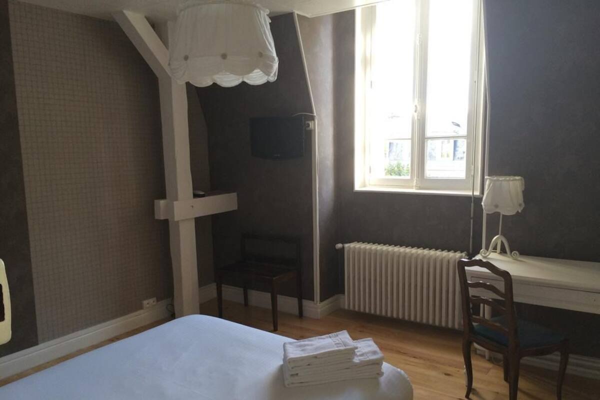 A bedroom with a bed, a desk, a chair, a radiator, and a window.