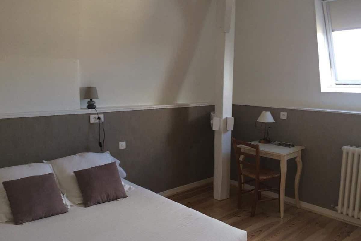 A bedroom with a bed, two pillows, a nightstand, a lamp, a chair, and a window.
