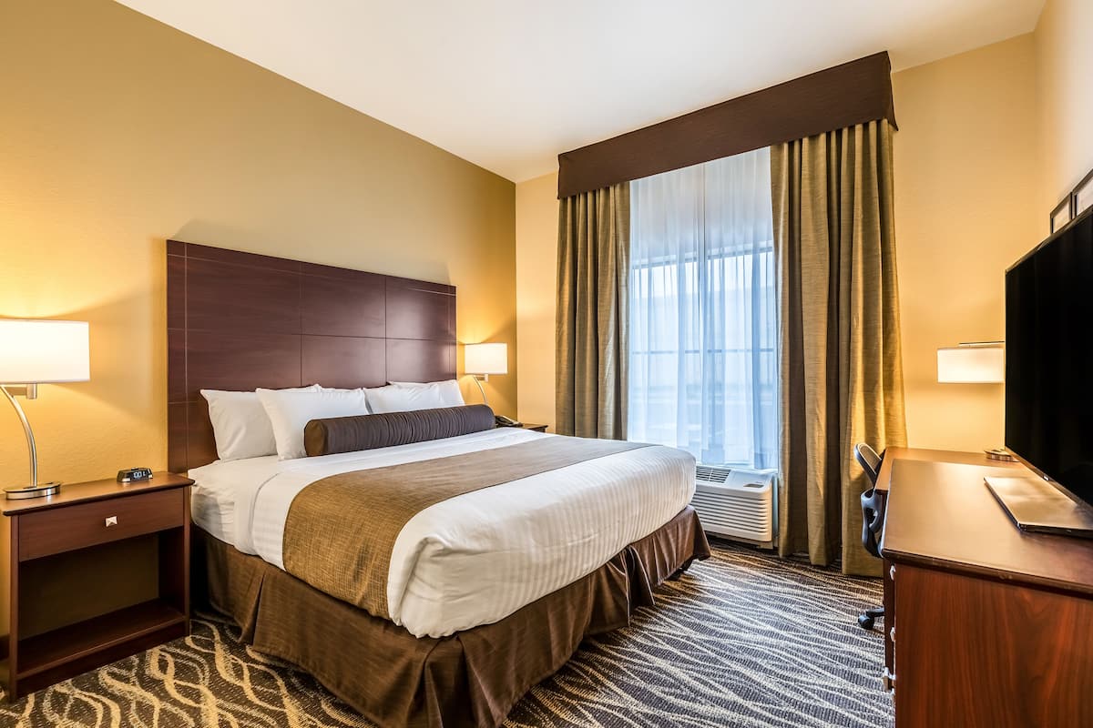 Een hotelkamer met een groot bed, een bureau met een televisie, een nachtkastje en een raam met gordijnen.