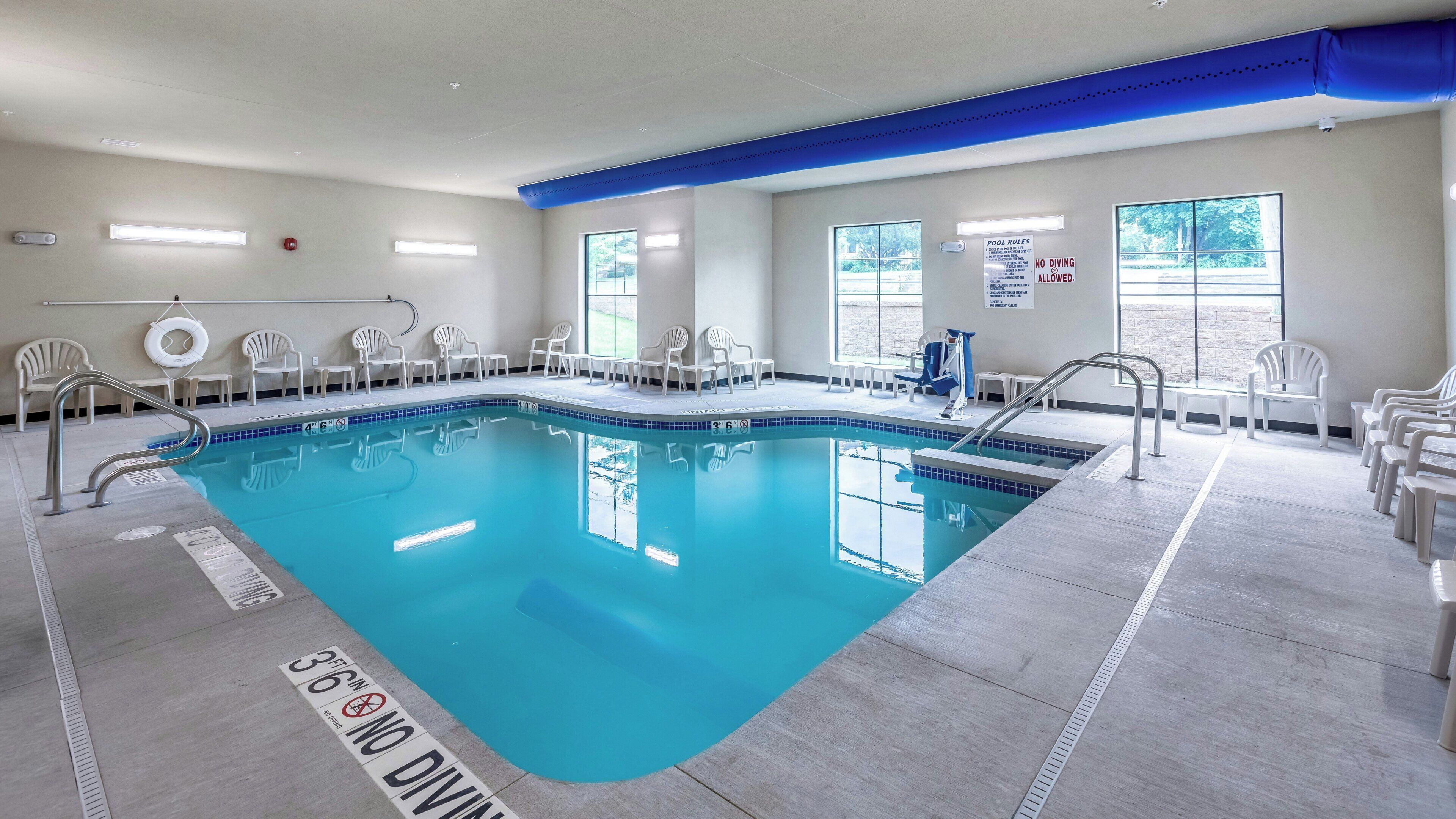 An indoor swimming pool with clear pool rules signage, a no diving sign, and a pool depth marker.