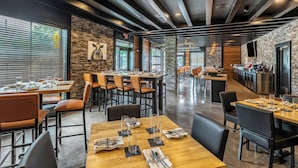 A modern restaurant with wooden tables, stone walls, and a bar area.