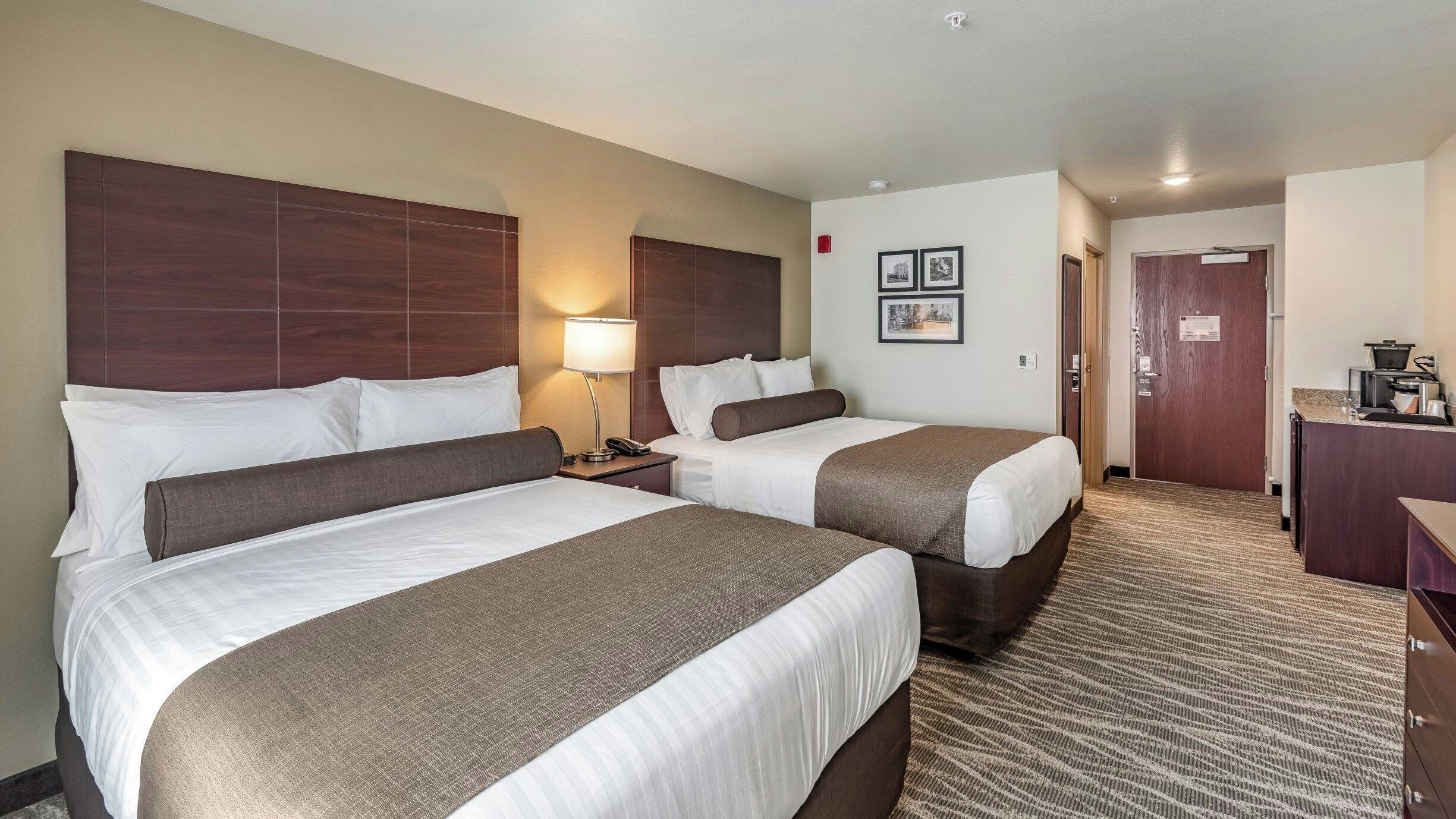 A hotel room with two beds, a desk, a lamp, and a door leading to a bathroom.