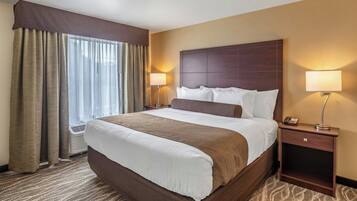 A hotel room with a large bed, two bedside lamps, a nightstand with a phone, and a window with curtains.