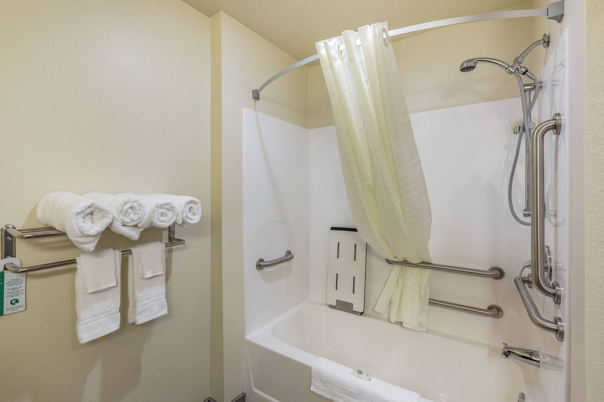 Een badkamer met een badkuip, douche en handgrepen. Handdoeken hangen aan een rek.