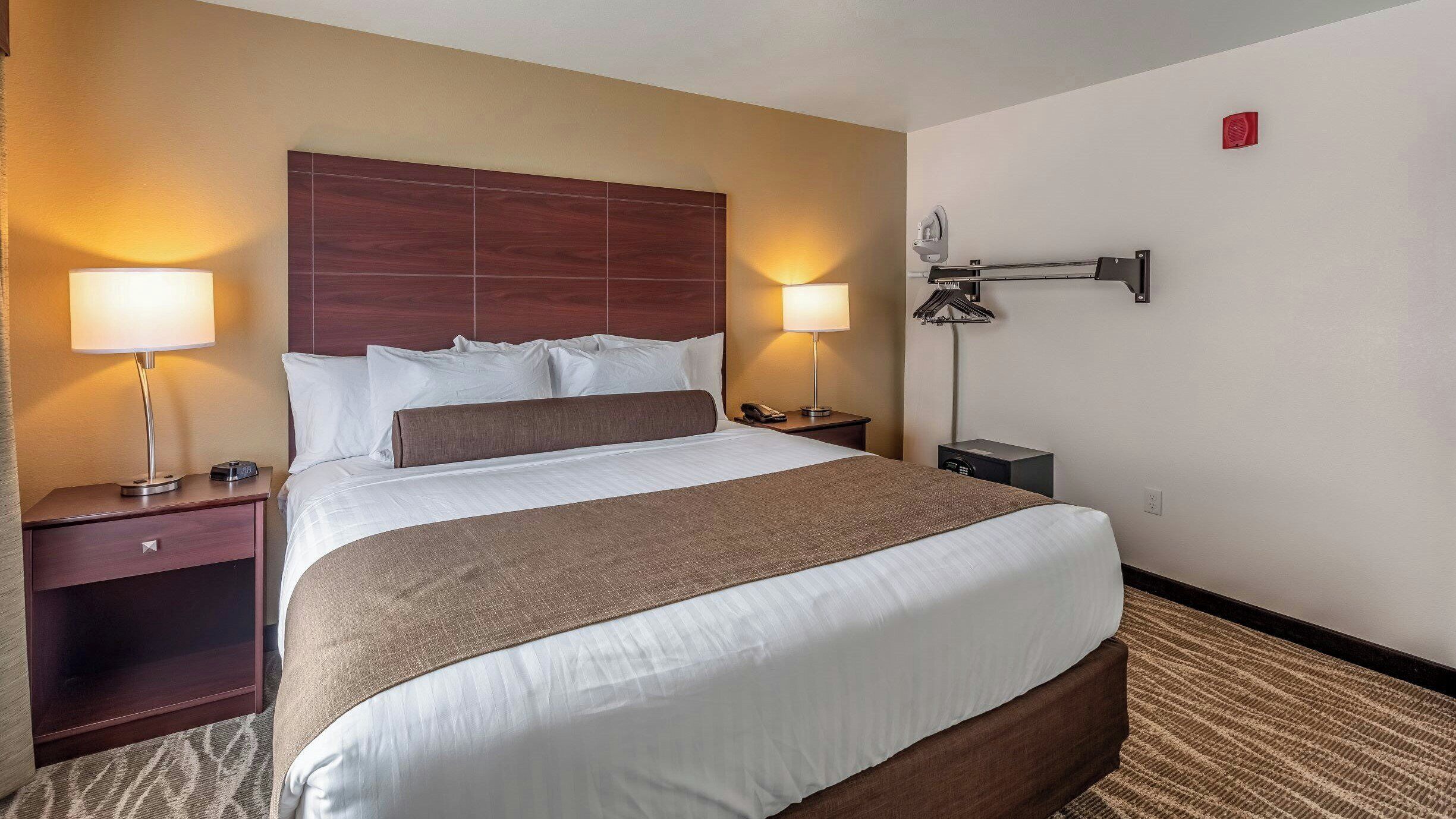 Una habitación de hotel con una cama grande, dos mesitas de noche, una lámpara de pared y un teléfono.