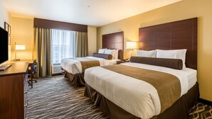 A hotel room with two beds, a desk, a TV, and a window with curtains.
