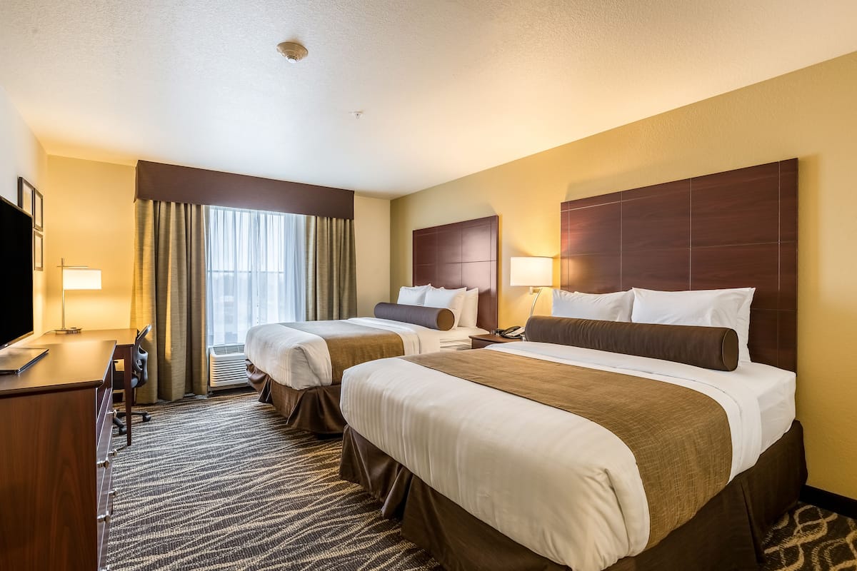 Een hotelkamer met twee bedden, een bureau, een televisie en een raam met gordijnen.