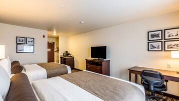 Ein Hotelzimmer mit zwei Betten, einem Schreibtisch, einem Sessel, einem Fernseher und gerahmten Bildern an der Wand.