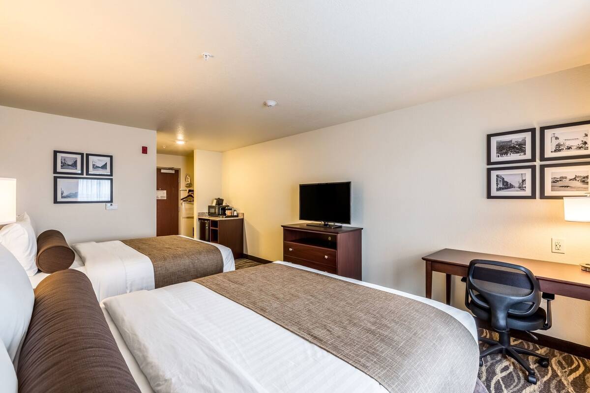 Een hotelkamer met twee bedden, een bureau, een televisie en een stoel.