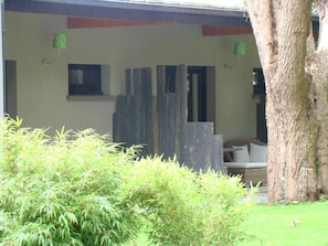 Un espacio al aire libre cubierto con estructura de madera, un árbol y follaje verde.