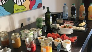 Un buffet proposant une variété de plats et de boissons, notamment des pots de confitures, un saladier de fruits et un tableau accroché au mur.