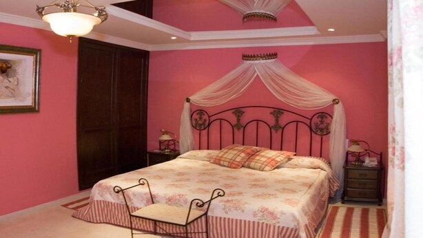 A bedroom with a canopy bed, a chair, a nightstand, and a lamp. - Hotel Mozart (Valladolid)