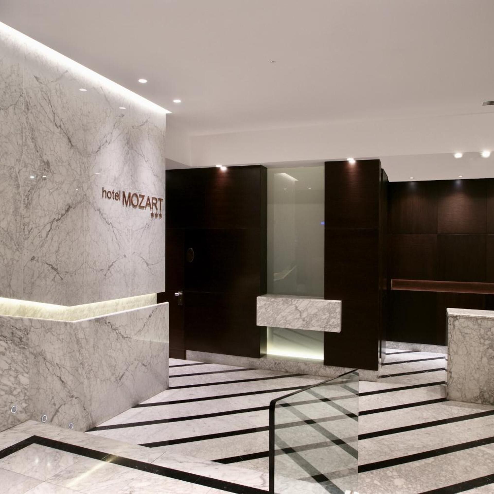 Un moderno vestíbulo de hotel con suelo de mármol, una recepción y un separador de vidrio.